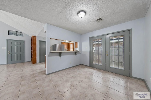 kitchen with a kitchen breakfast bar, kitchen peninsula, stainless steel fridge, vaulted ceiling, and a textured ceiling