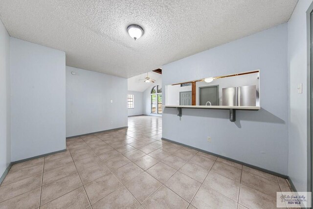 tiled spare room with lofted ceiling, ceiling fan, and a textured ceiling