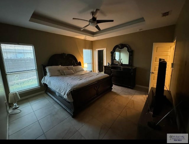 bedroom with a tray ceiling, visible vents, a ceiling fan, and light tile patterned flooring