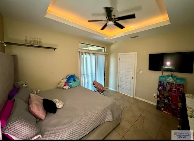 bedroom featuring a tray ceiling, visible vents, a ceiling fan, and baseboards