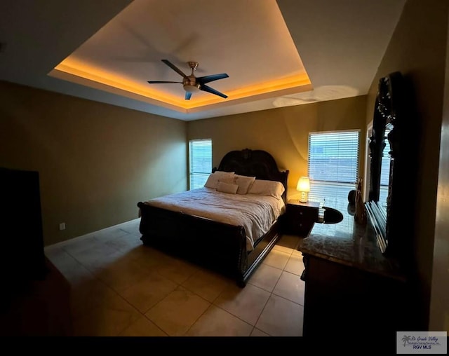 bedroom with a ceiling fan, a tray ceiling, and light tile patterned flooring