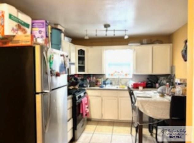 kitchen featuring light tile patterned flooring, stainless steel fridge, rail lighting, and black gas range oven