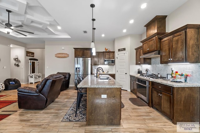 kitchen with appliances with stainless steel finishes, light stone counters, sink, a center island with sink, and decorative light fixtures