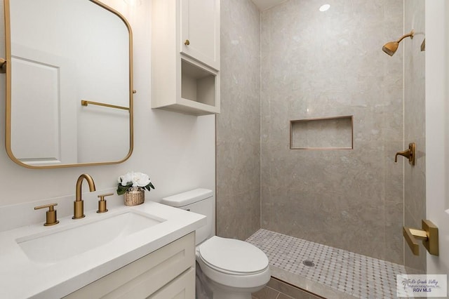 bathroom with toilet, vanity, and a tile shower