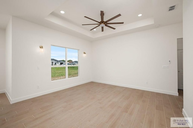 spare room featuring ceiling fan, a raised ceiling, and light wood-type flooring