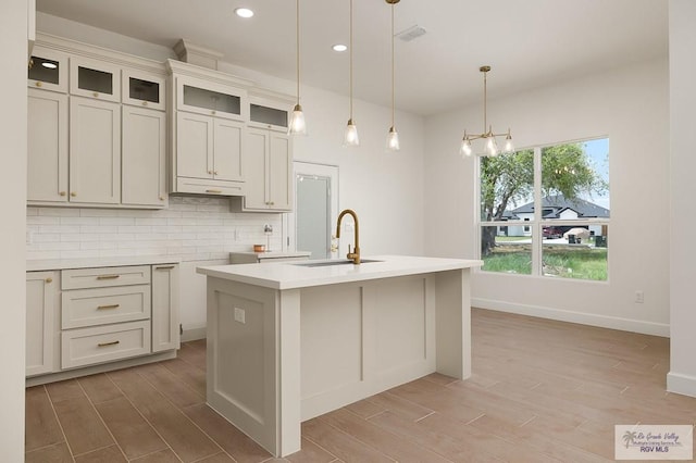 kitchen featuring decorative light fixtures, backsplash, a notable chandelier, a center island with sink, and sink