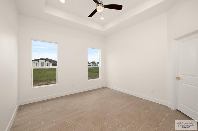 empty room with ceiling fan and a raised ceiling