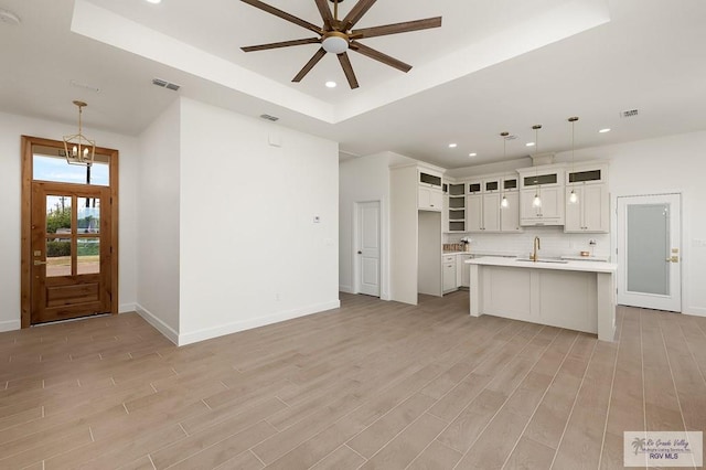 kitchen featuring white cabinets, a kitchen island with sink, decorative backsplash, and pendant lighting