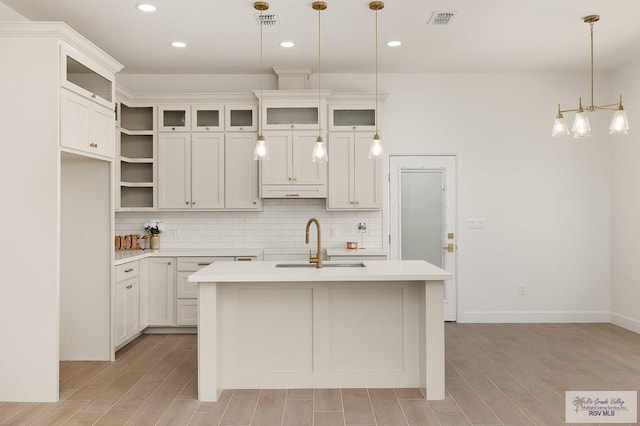 kitchen featuring a center island with sink, tasteful backsplash, hanging light fixtures, white cabinets, and sink