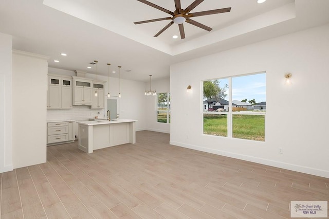 kitchen with ceiling fan with notable chandelier, pendant lighting, decorative backsplash, a raised ceiling, and a center island with sink