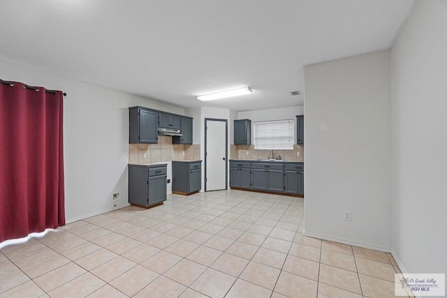 3017 Paradise Ave, Harlingen, TX 78552 - kitchen featuring decorative backsplash, gray cabinetry, under cabinet range hood, light tile patterned floors, and a sink