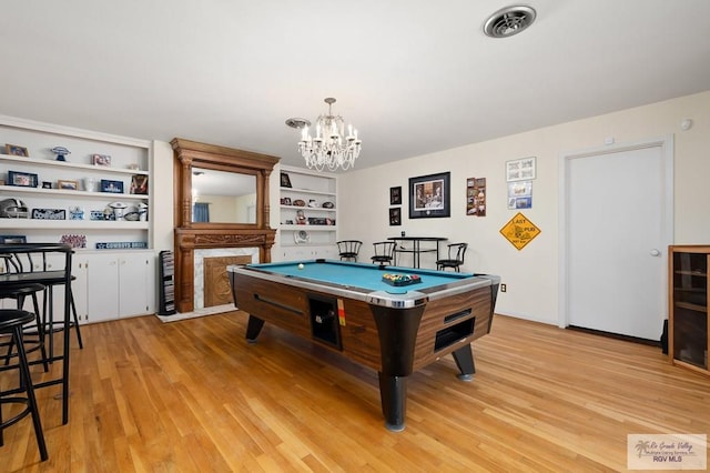 playroom with built in shelves, light wood-type flooring, a fireplace, pool table, and a chandelier