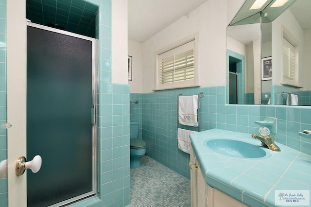 bathroom featuring tile patterned floors, vanity, a shower with shower door, and tile walls