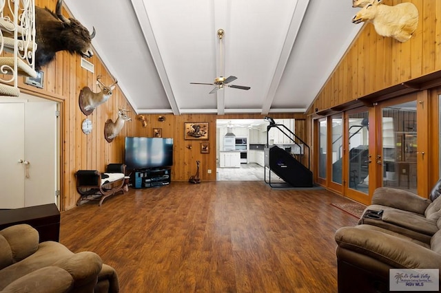 living room featuring ceiling fan, french doors, vaulted ceiling with beams, wood walls, and wood-type flooring