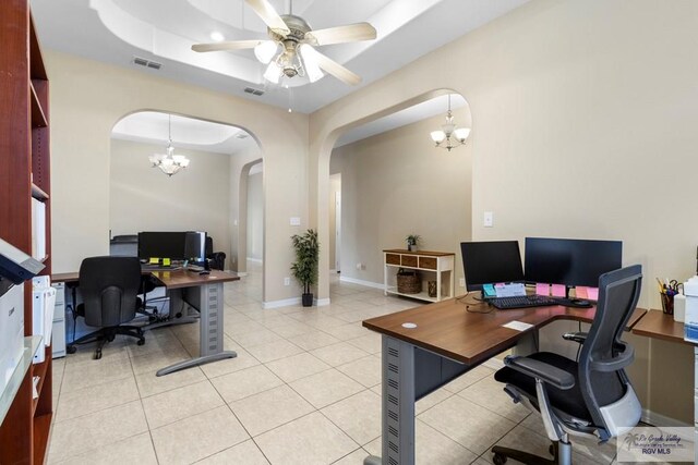 office space with light tile patterned floors, ceiling fan with notable chandelier, and a tray ceiling