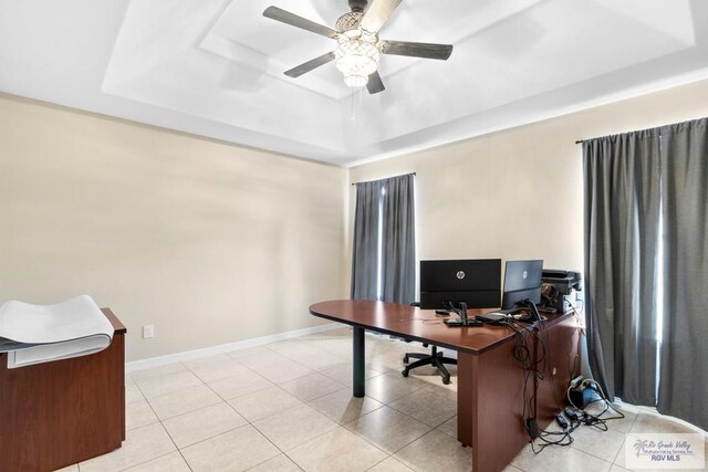 office space with light tile patterned floors, a raised ceiling, and ceiling fan