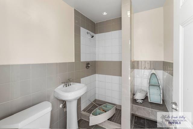 bathroom with a tile shower, toilet, and tile walls