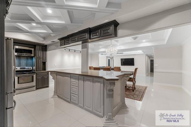 kitchen with stainless steel appliances, a kitchen island, a notable chandelier, and light tile patterned flooring