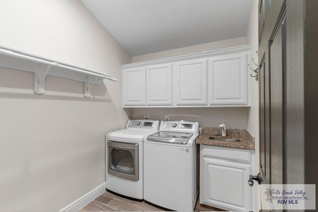 laundry area featuring washer and clothes dryer, light hardwood / wood-style floors, cabinets, and sink