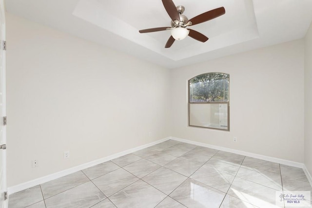 empty room with ceiling fan, light tile patterned flooring, and a raised ceiling