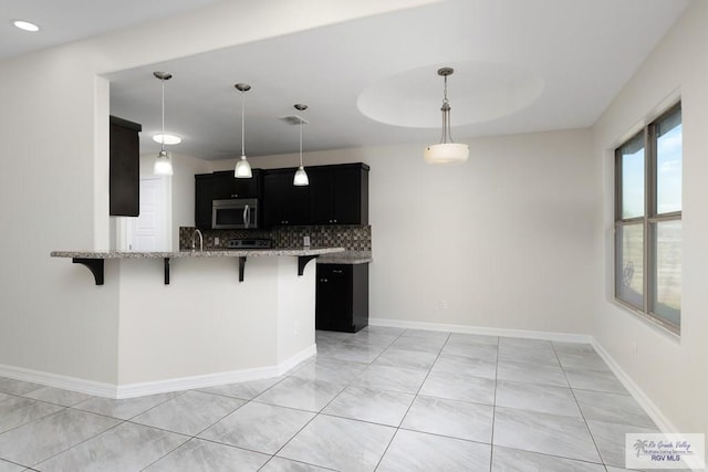 kitchen featuring decorative backsplash, kitchen peninsula, light stone counters, hanging light fixtures, and a breakfast bar area