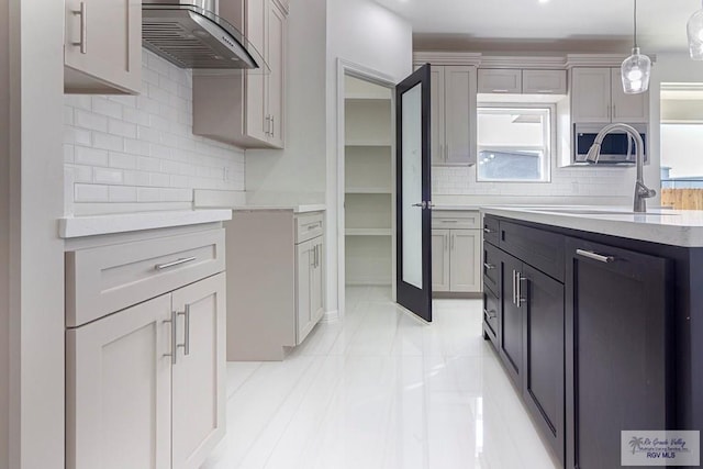 kitchen with extractor fan, a sink, light countertops, hanging light fixtures, and backsplash