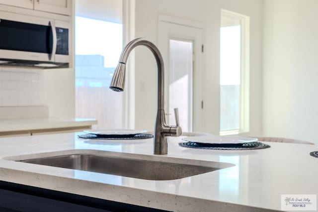 interior details with white microwave, light stone counters, decorative backsplash, and a sink