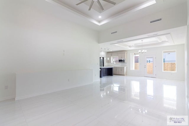 unfurnished living room with ceiling fan with notable chandelier, a raised ceiling, visible vents, and baseboards