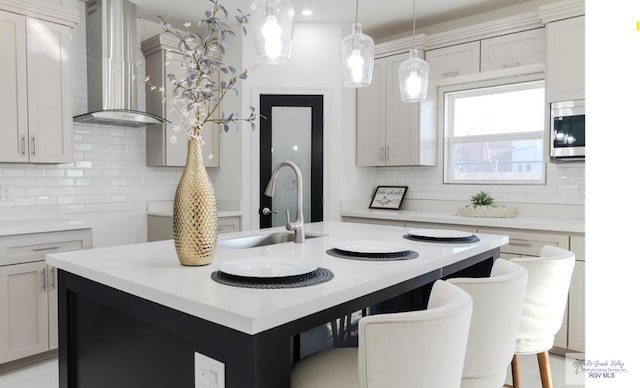 kitchen featuring wall chimney range hood, stainless steel microwave, light countertops, and a sink