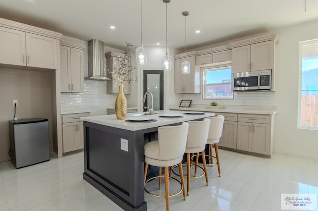 kitchen with a center island with sink, wall chimney exhaust hood, a breakfast bar, stainless steel appliances, and a sink