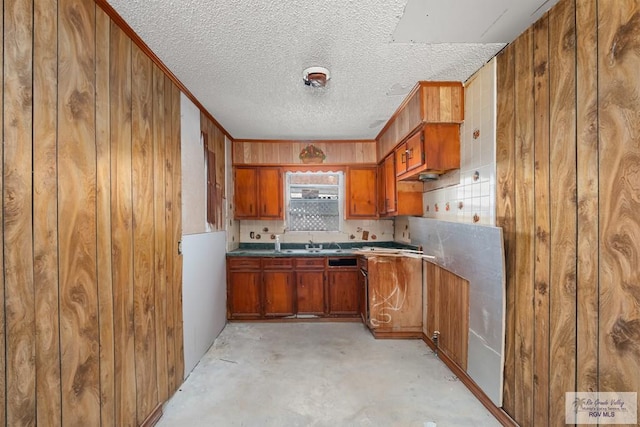 kitchen with a textured ceiling, sink, backsplash, and wooden walls