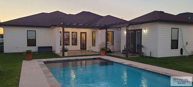 back house at dusk featuring a lawn and a patio