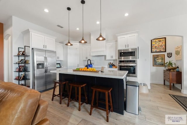 kitchen featuring a breakfast bar, stainless steel appliances, a kitchen island with sink, white cabinets, and hanging light fixtures