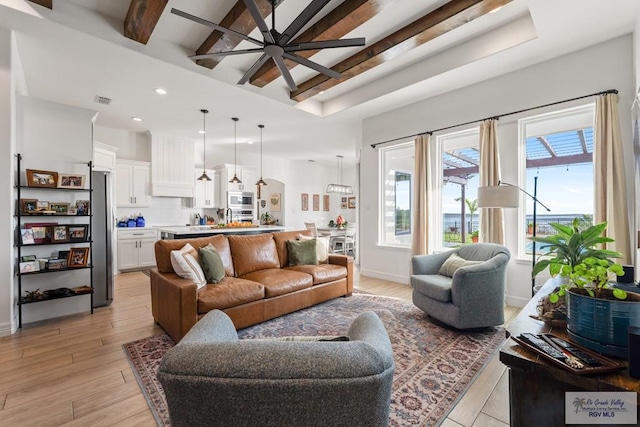 living room featuring beam ceiling, light wood-type flooring, ceiling fan, and a healthy amount of sunlight