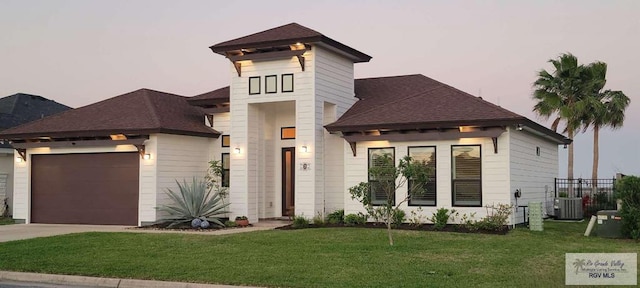 view of front of home with a lawn, cooling unit, and a garage