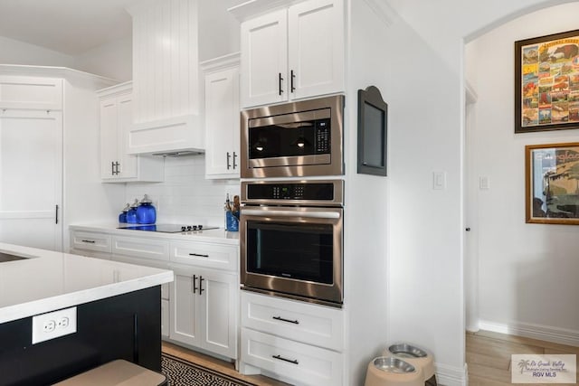 kitchen with backsplash, white cabinets, light hardwood / wood-style floors, and appliances with stainless steel finishes