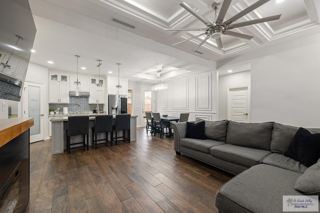 living room with dark hardwood / wood-style flooring, a raised ceiling, ceiling fan, crown molding, and coffered ceiling