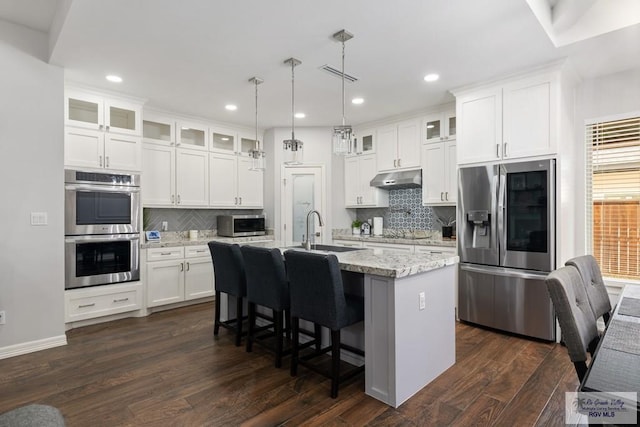 kitchen featuring sink, an island with sink, stainless steel appliances, white cabinets, and light stone counters