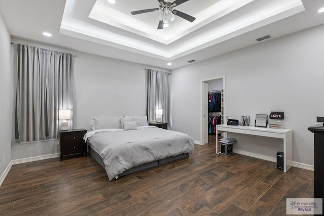 bedroom with ceiling fan, a walk in closet, a closet, and a raised ceiling