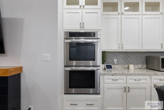 kitchen featuring decorative backsplash, stainless steel double oven, and white cabinets