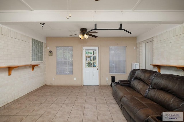 living room featuring ceiling fan, light tile patterned floors, and brick wall