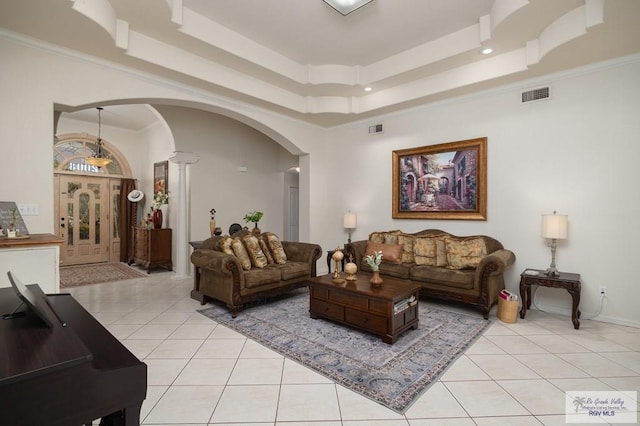 living room featuring light tile patterned floors, a tray ceiling, decorative columns, and ornamental molding