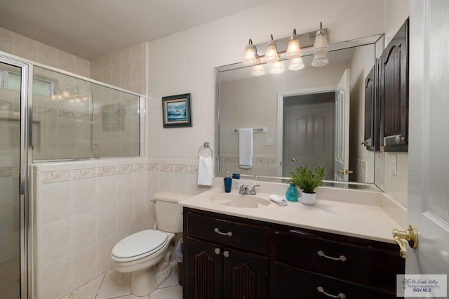 bathroom featuring tile patterned flooring, toilet, vanity, a shower with shower door, and tile walls