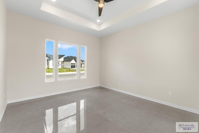 tiled empty room with ceiling fan and a tray ceiling