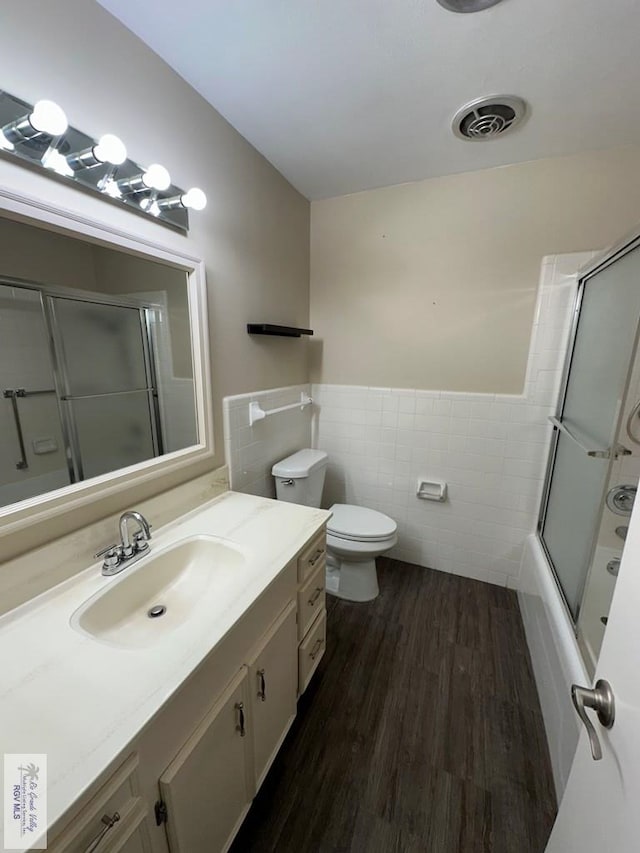 full bathroom featuring combined bath / shower with glass door, tile walls, hardwood / wood-style floors, vanity, and toilet