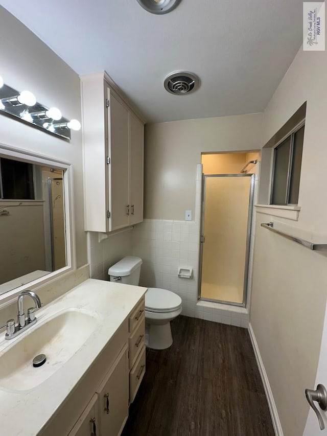 bathroom with toilet, a shower with shower door, tile walls, vanity, and hardwood / wood-style floors