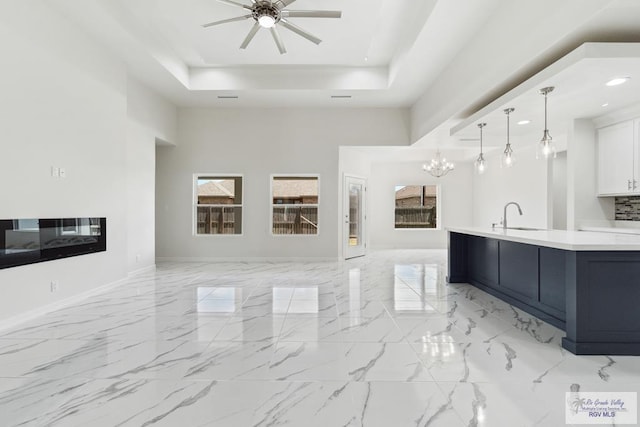 kitchen with white cabinetry, hanging light fixtures, sink, ceiling fan with notable chandelier, and a tray ceiling