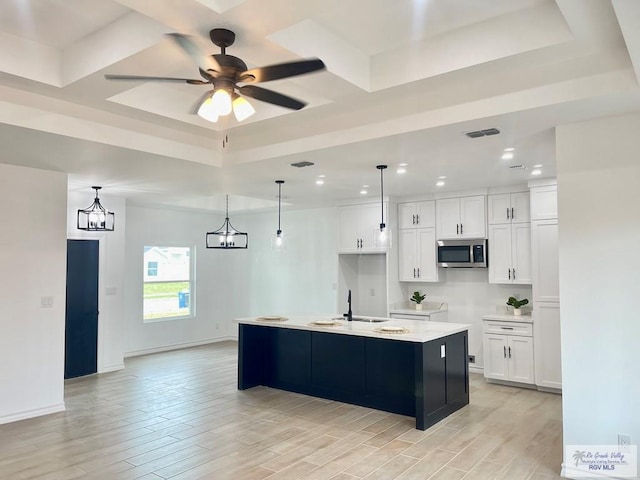 kitchen with sink, white cabinetry, hanging light fixtures, a center island with sink, and a raised ceiling