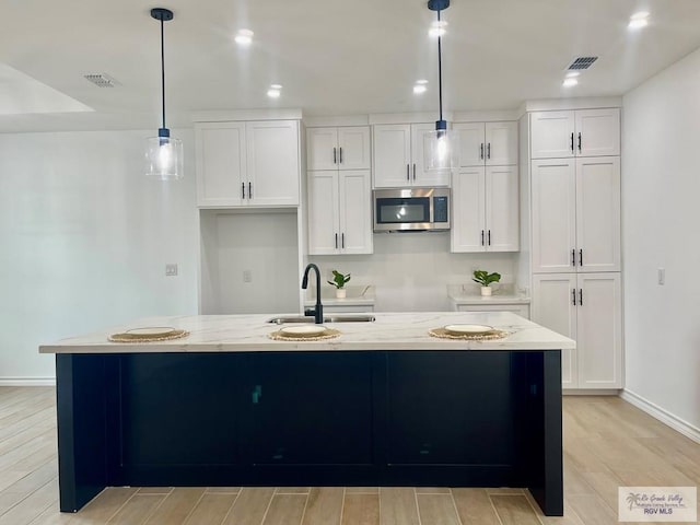 kitchen featuring hanging light fixtures, a kitchen island with sink, sink, and white cabinets