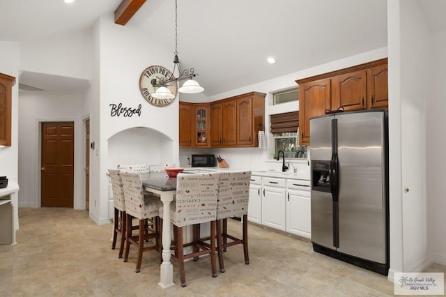 kitchen featuring stainless steel fridge with ice dispenser, a kitchen breakfast bar, light countertops, high vaulted ceiling, and beam ceiling